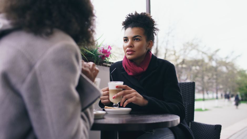 Two friends talking over coffee at a sunny outdoor café
