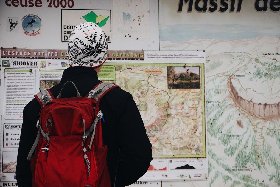 A hiker with a backpack studying a trail map in front of the mountains